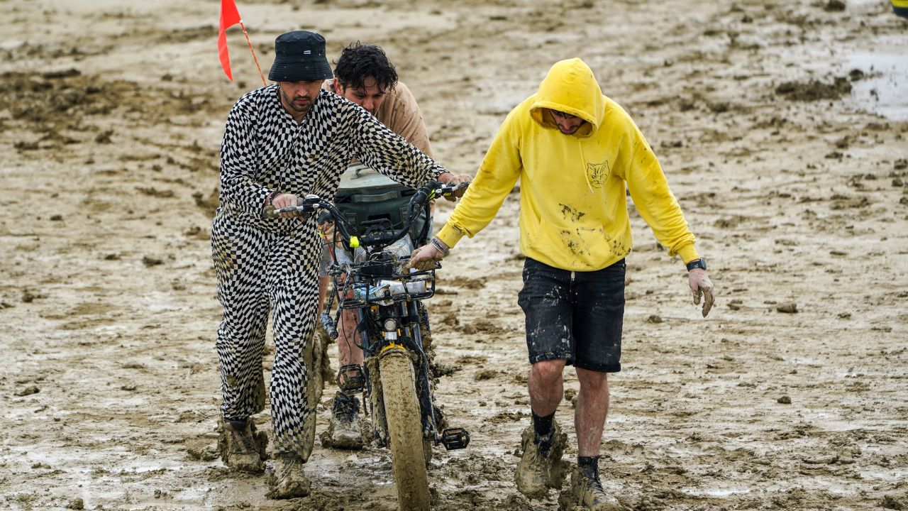 People at Burning Man push an e-bike through thick mud.