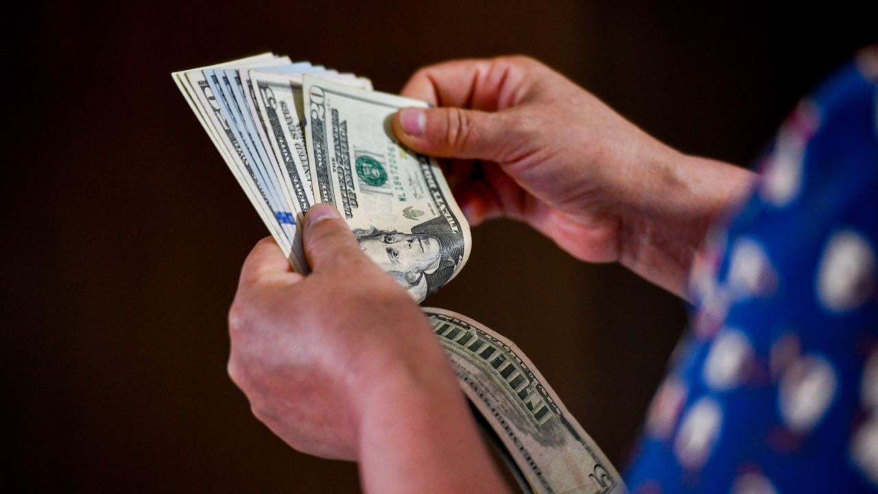 In this photo illustration, a person seen holding 5 and 20 US dollar bills in his hand.