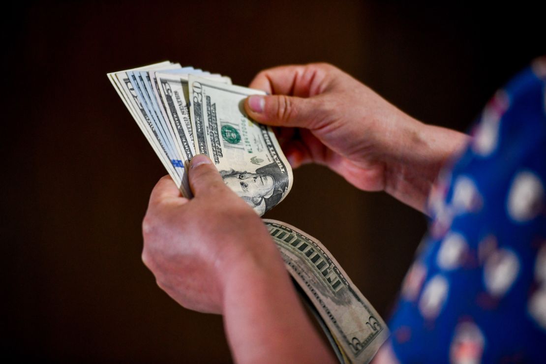 In this photo illustration, a person seen holding 5 and 20 US dollar bills in his hand.