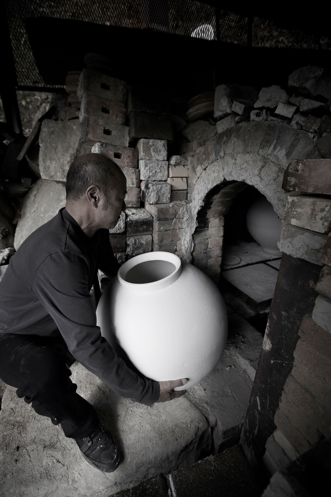 Kwon Dae Sup lifts a large moon jar into a kiln.