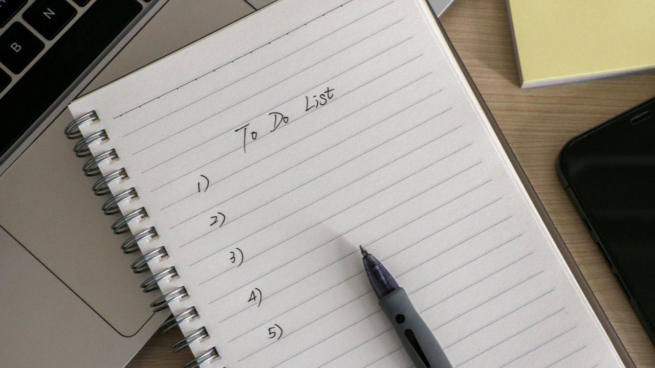 Organization and To Do List concept, workplace with notepad, ballpoint pen, some sticky notes, a laptop and smartphone, on wooden desk. Checklist for work and life.