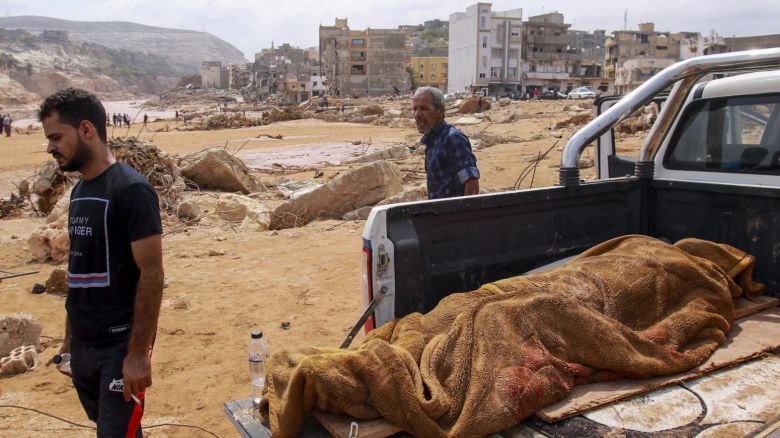 People walk past the body of a flash flood victim in the back of a pickup truck in Derna, eastern Libya, on Monday.