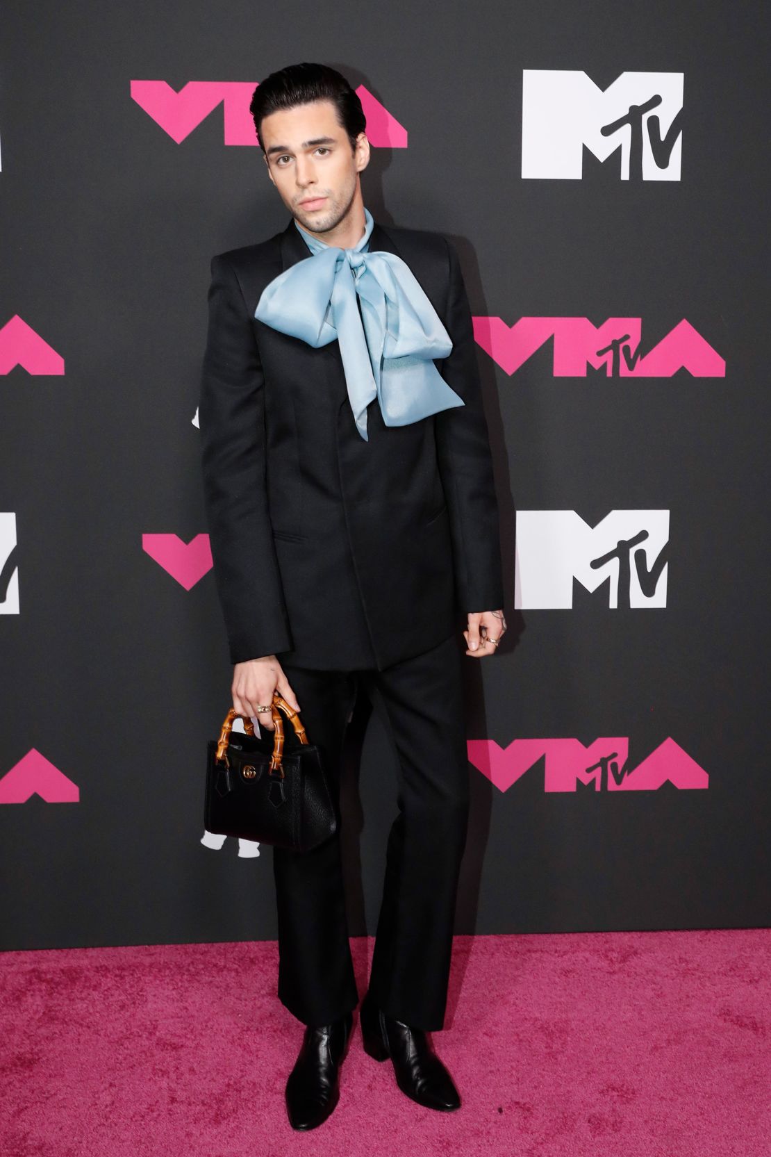 Up-and-coming singer-songwriter Stephen Sanchez was all wrapped up in a black suit with an oversized baby-blue bow, a black Gucci bamboo handle Diana tote bag and black leather boots. 