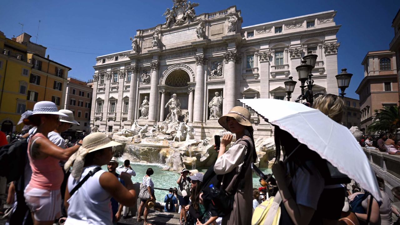 Tourists protect themselves with hats and umbrellas at the Trevi Fountain during a heat wave in Rome, August 21, 2023. (Photo by Filippo MONTEFORTE / AFP) (Photo by FILIPPO MONTEFORTE/AFP via Getty Images)