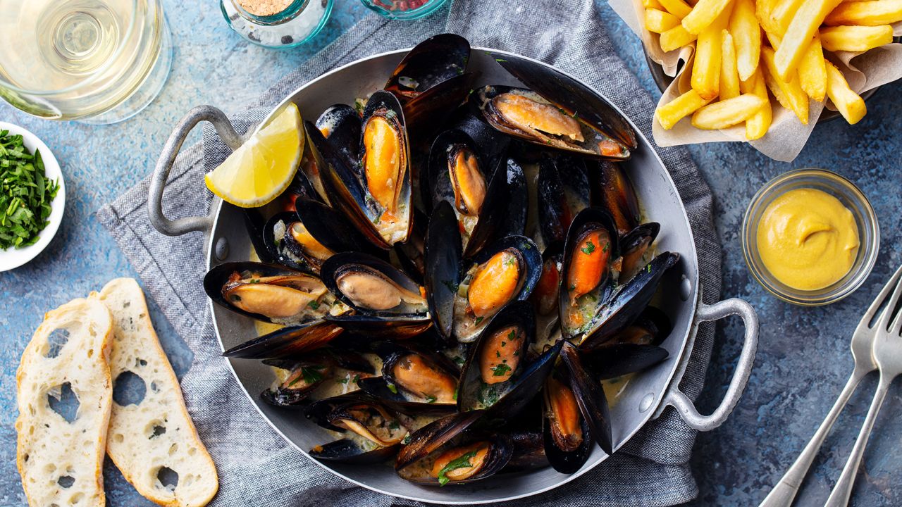 Mussels with french fries and white wine in cooking pan. Grey background. Close up. Top view.