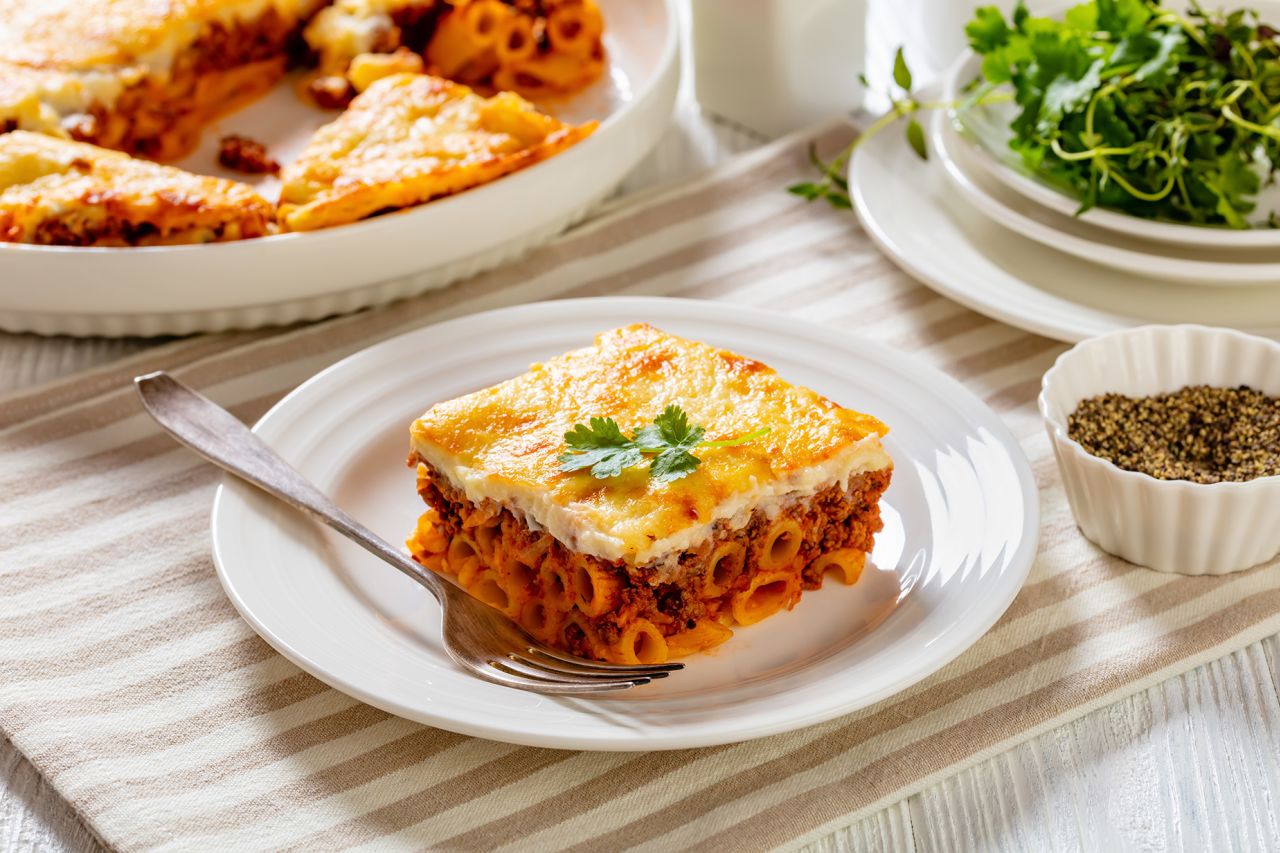 Greek Pastitsio of pasta, ground lamb, grated cheese, and tomatoes topped with bechamel sauce and melted cheese on white plate