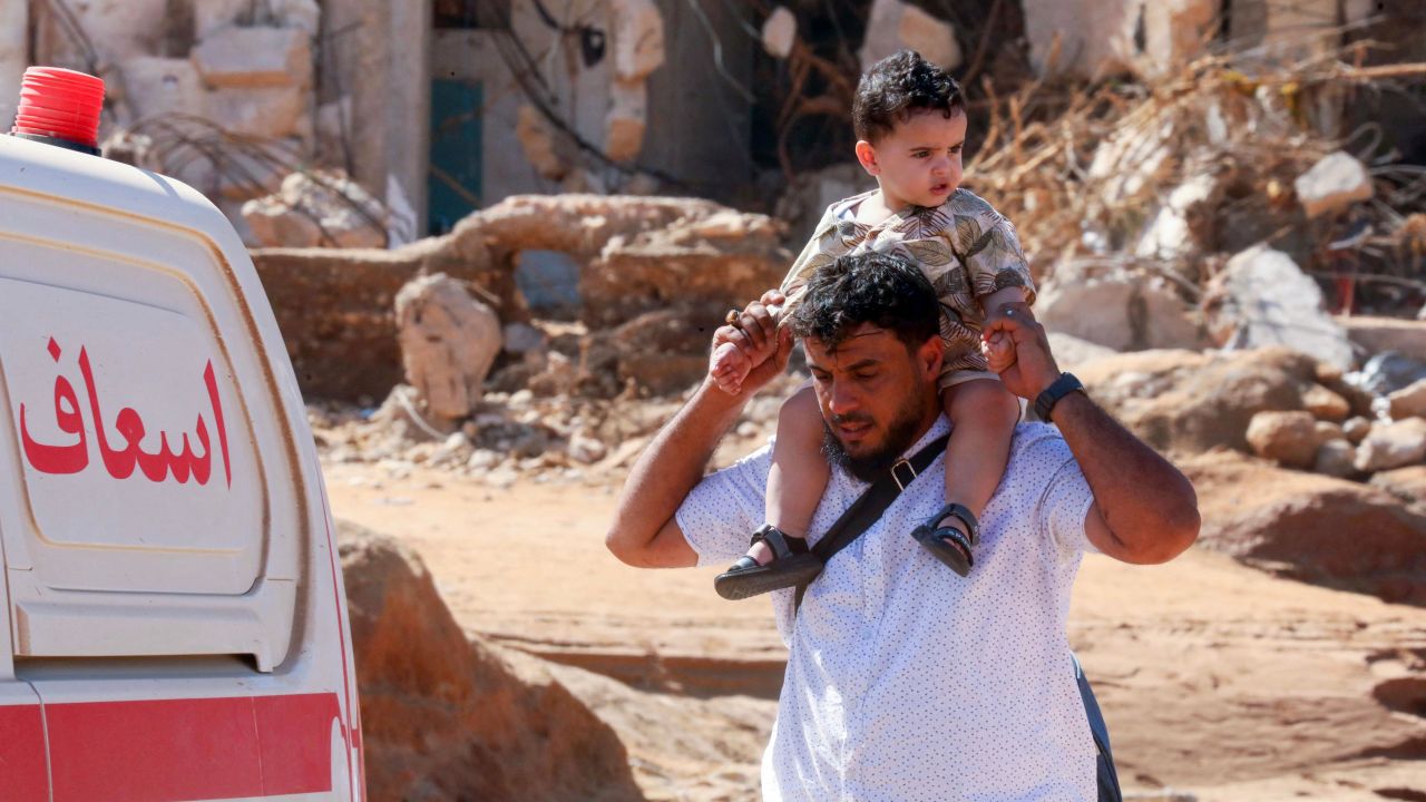 A man carries a child on his shoulder as he walks past a flash flood-damaged area in Derna on September 14, 2023.