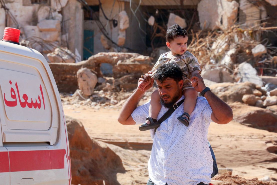 A man carries a child on his shoulder as he walks past a flash flood-damaged area in Derna on September 14, 2023.