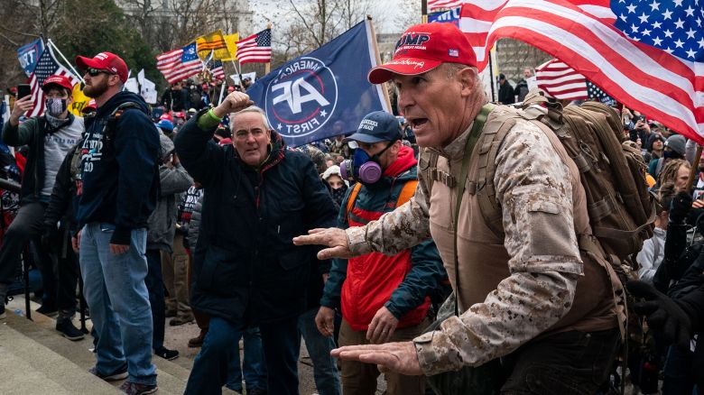 Ray Epps, in the red Trump hat, center, gestures to a line of law enforcement officers, as people gather on the West Front of the U.S. Capitol on Wednesday, Jan. 6, 2021 in Washington, DC.