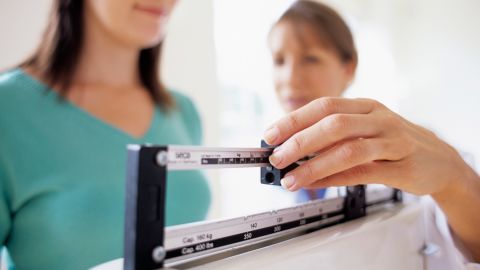 Weight check-up. General practice doctor adjusting the balance on weighing scales while weighing a young female patient. Weight is an important indicator of general health.