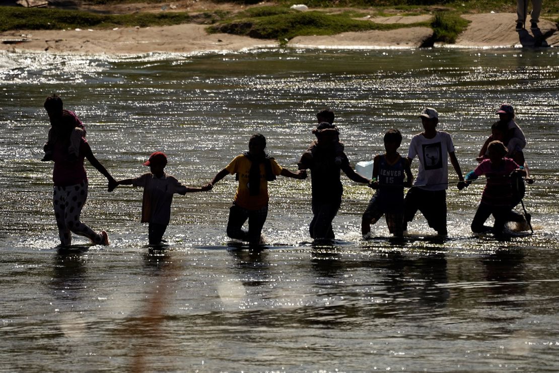 Migrants join hands as they cross the Rio Grande from Mexico into the US, on Thursday, Sept. 21, 2023, in Eagle Pass, Texas.