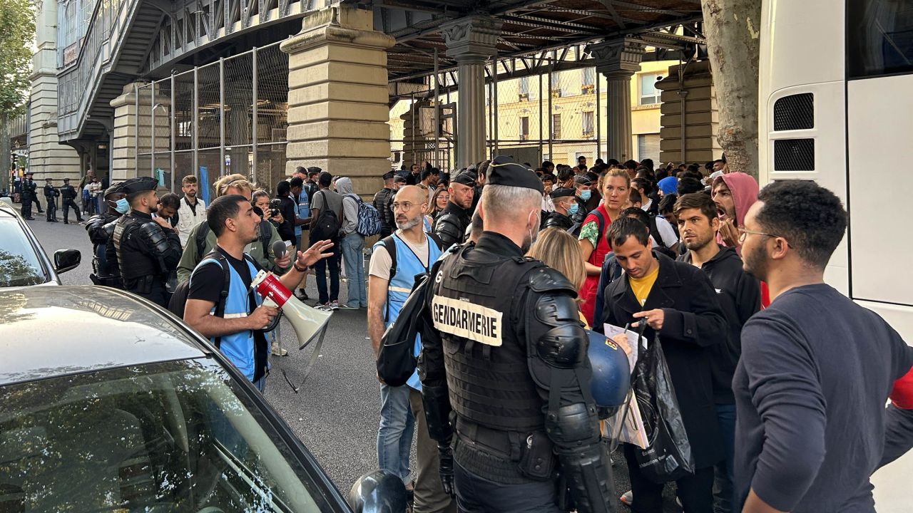 Police and workers from humanitarian organizations talk to those waiting to board a bus by the homeless camp in Paris.