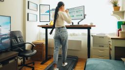 Woman working from home at standing desk is walking on under desk treadmill