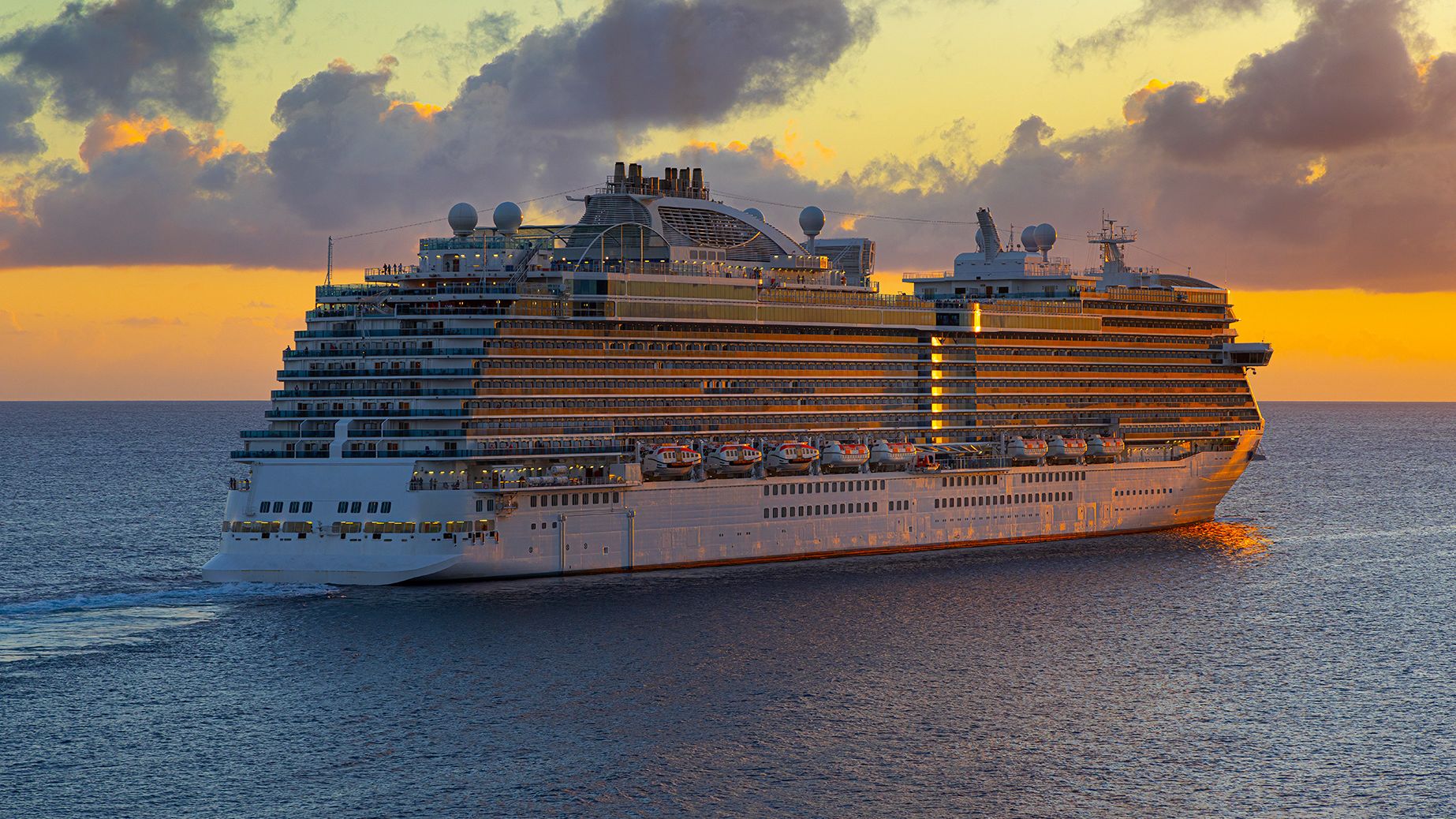 Cruise ship sailing off into fiery tropical sunset.