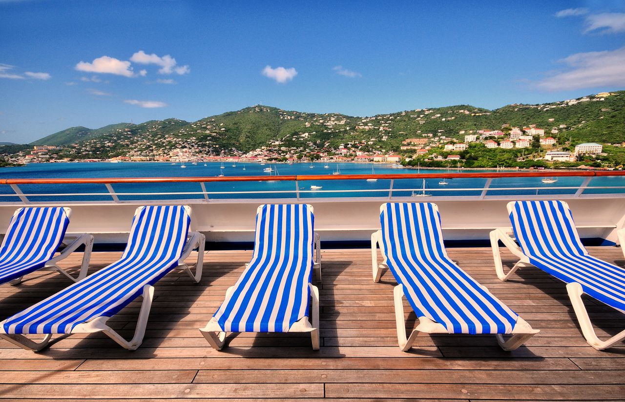 Empty lounge chairs on the top deck of a cruise ship overlooking a tropical island in the Caribbean