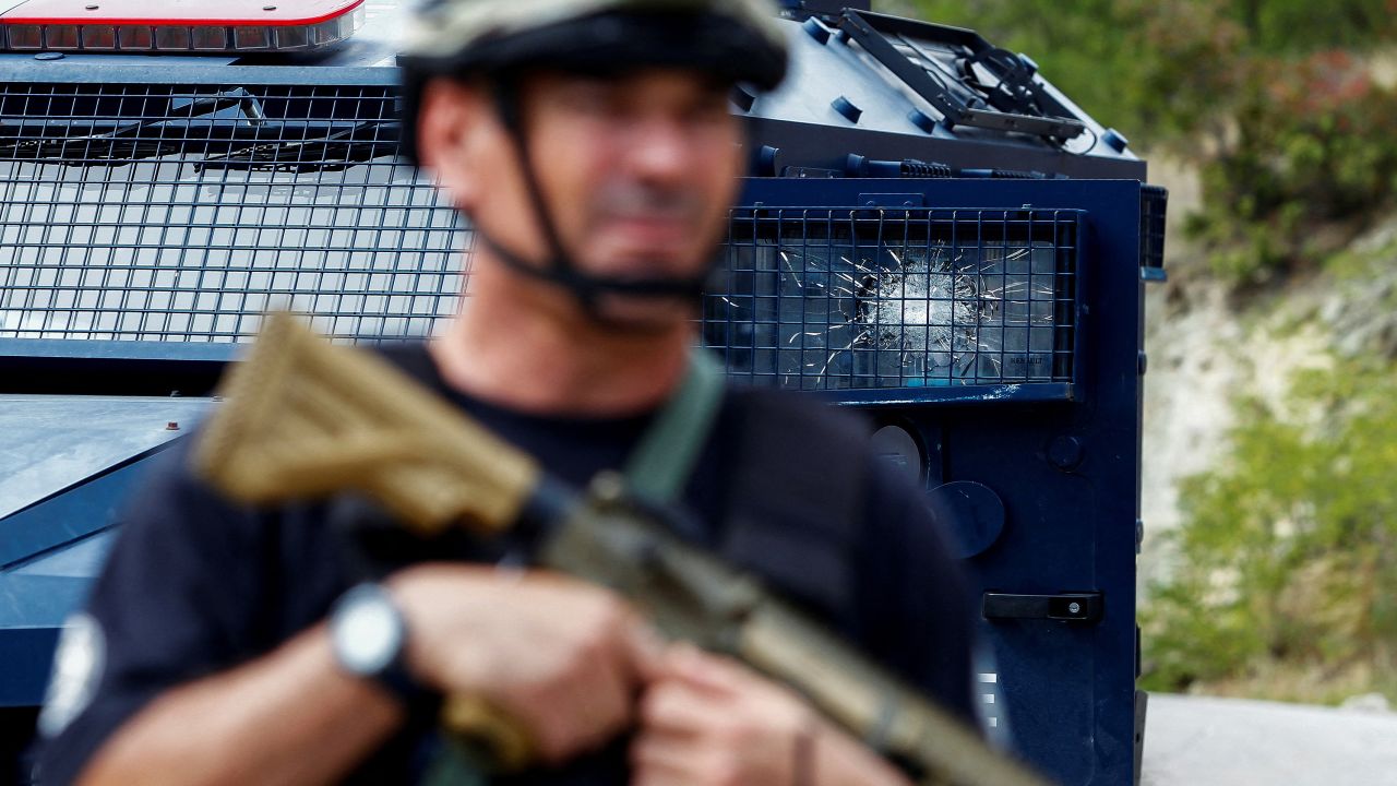 A Kosovo police officer stands guard in front of a vehicle with a cracked window in Banjska.