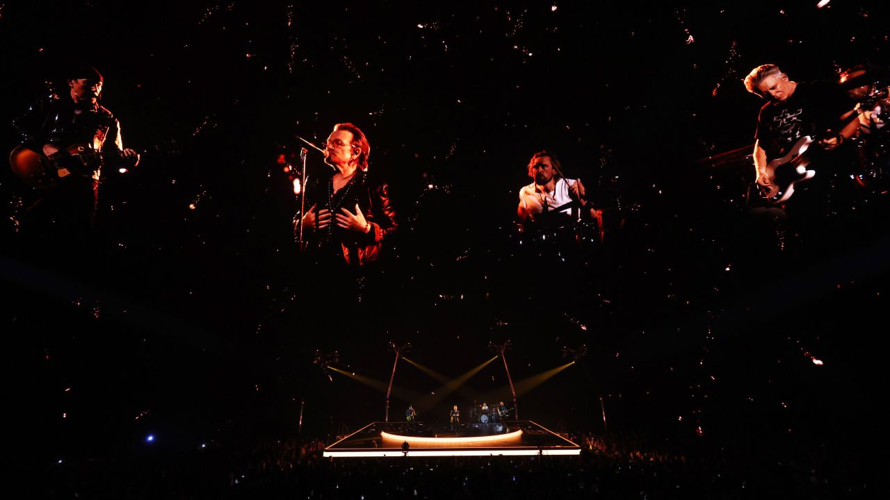 Enormes imágenes en vivo de Bono, The Edge, Adam Clayton y Bram van den Berg de U2 se proyectan en la pantalla.