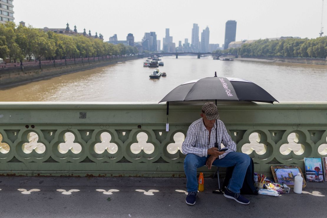 An artist sits beneath the shade of an umbrella on Westminster Bridge during hot weather in London on September 6.
