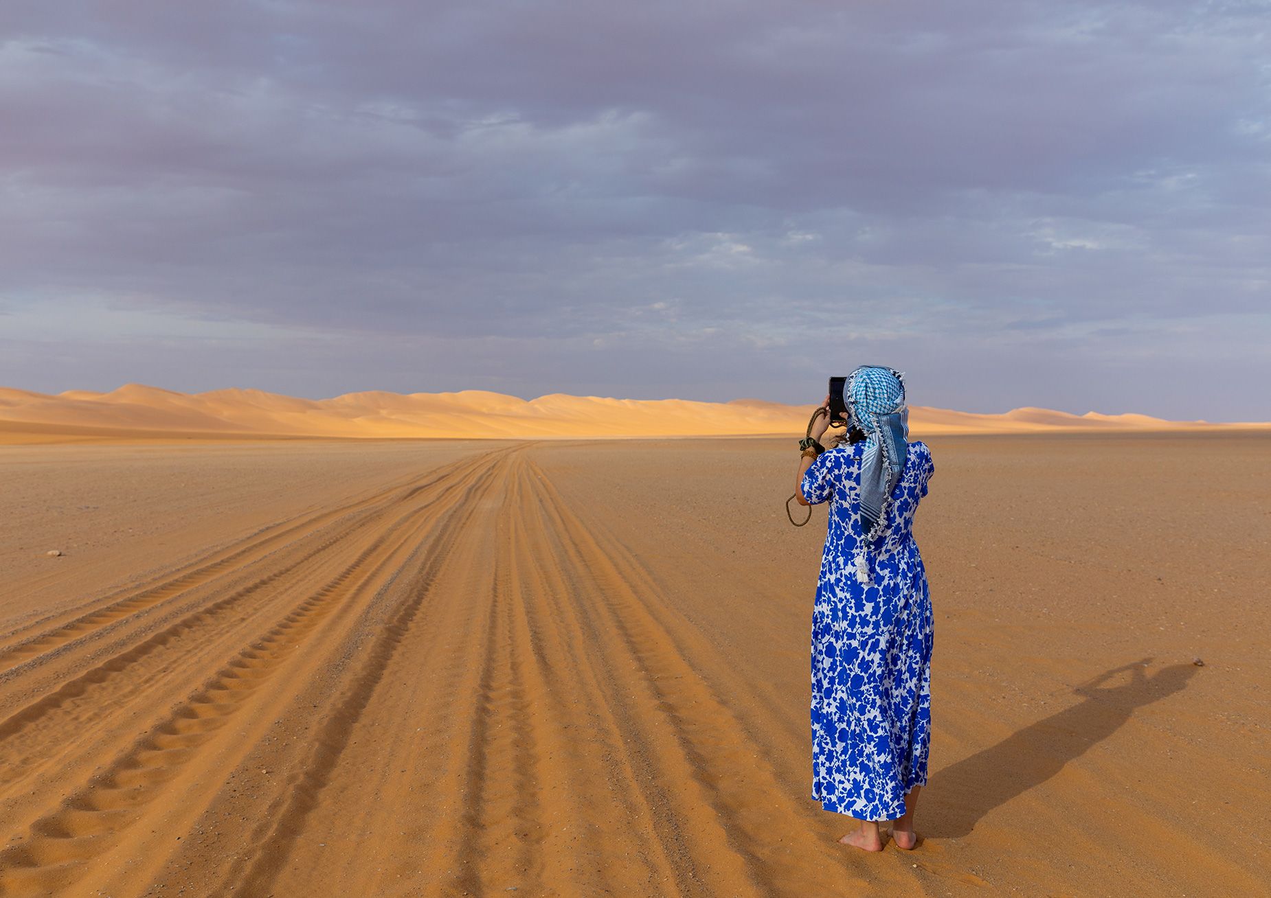 A woman in long dress and head scarf takes a photo of a Rub al Khali sand dune in Saudi Arabia