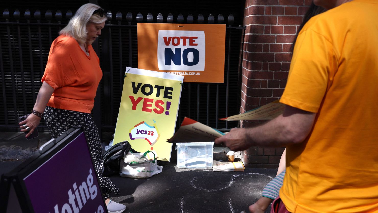 A woman walks past volunteers handing out voting brochures outside a voting center in central Sydney on October 3, 2023.