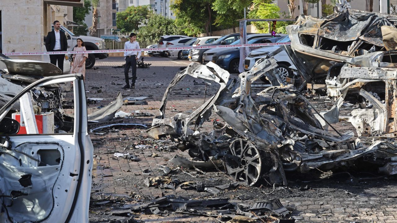 Residents look at the wreckage of destroyed vehicles in Ashkelon, a coastal city in southern Israel, following a rocket attack from the Gaza Strip.