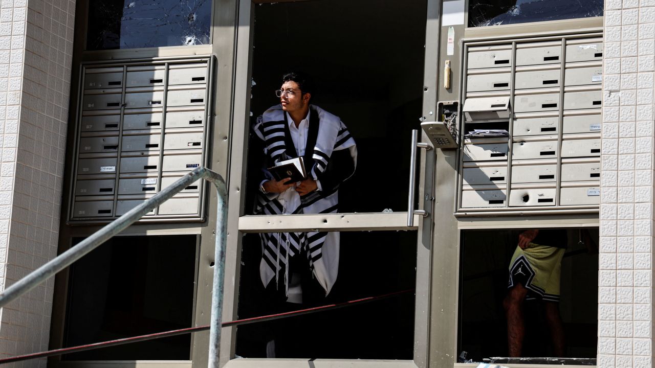 A man wearing a Jewish prayer shawl looks out of the damaged entranceway to a building, as rockets are launched from the Gaza Strip, in Ashkelon, southern Israel.