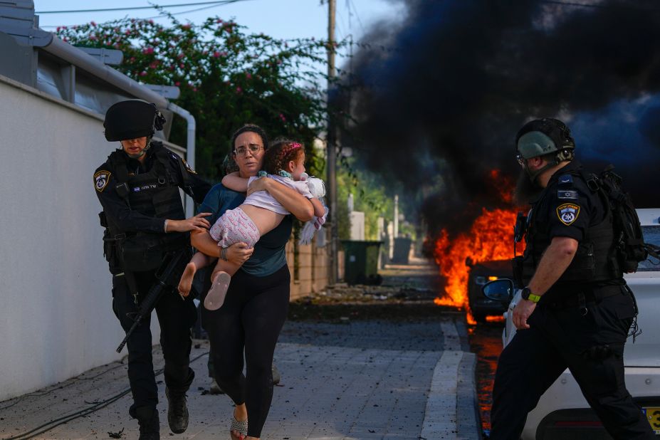 Police officers evacuate a woman and a child from a site hit by a rocket in Ashkelon, Israel, on Saturday, October 7.