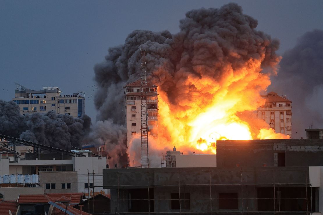 People standing on a rooftop watch as a ball of fire and smoke rises above a building in Gaza City on October 7, 2023 during an Israeli air strike. At least 70 people were reported killed in Israel, while Gaza authorities released a death toll of 198 in the bloodiest escalation in the wider conflict since May 2021, with hundreds more wounded on both sides.