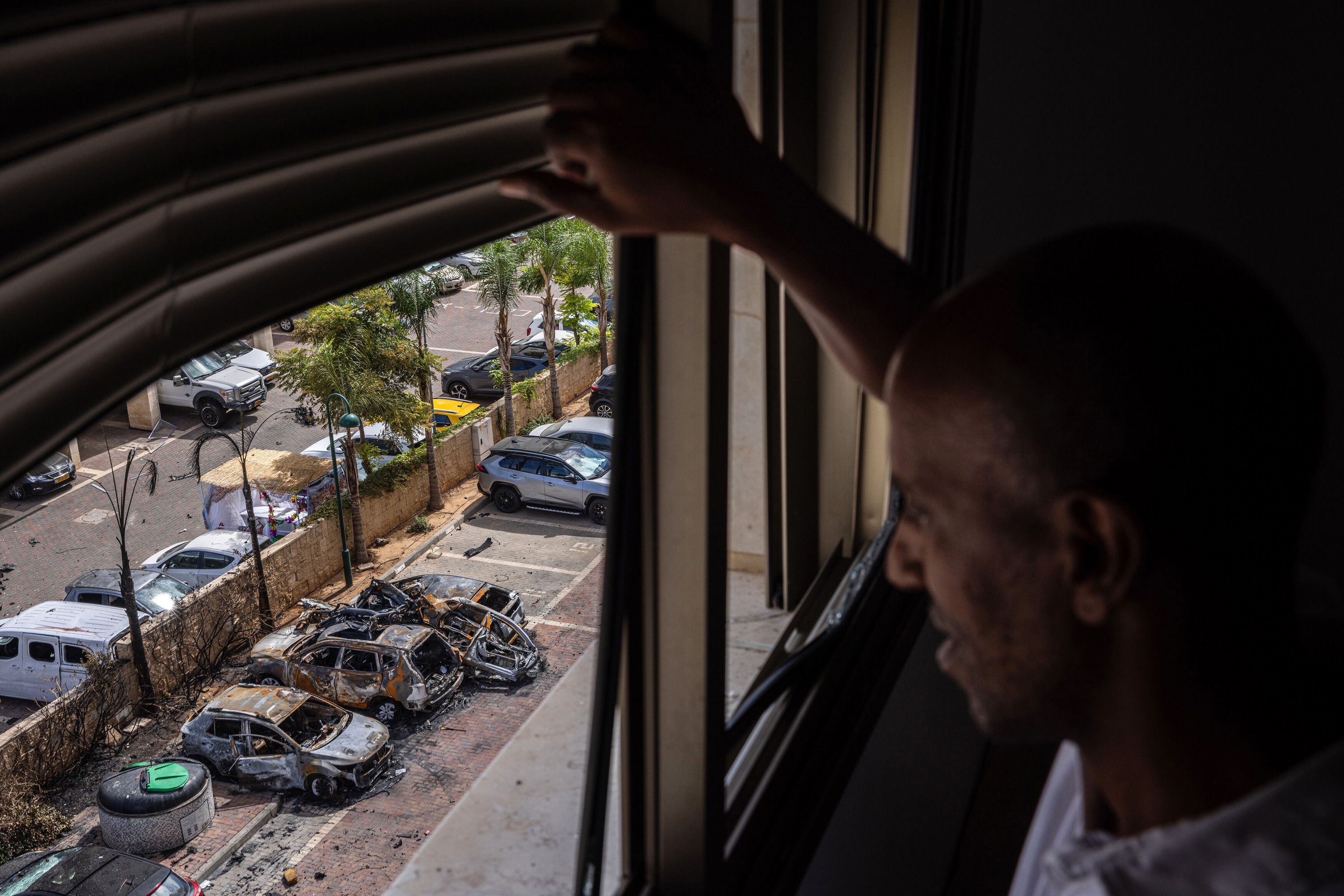 From the window of his family's apartment, a man surveys damage from a rocket that struck a parking lot in Ashkelon on October 7.