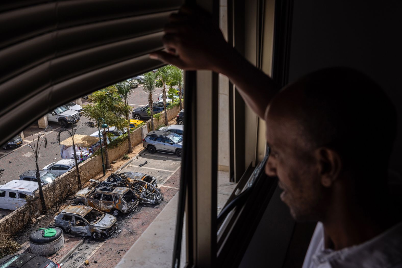 From the window of his family's apartment, a man surveys damage from a rocket that struck a parking lot in Ashkelon, Israel, on Saturday, October 7.