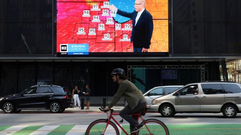 A bicyclist rides past a screen airing a news channel showing a weather segment forecasting an upcoming heat wave on Aug. 22, 2023, at Daley Plaza in Chicago.