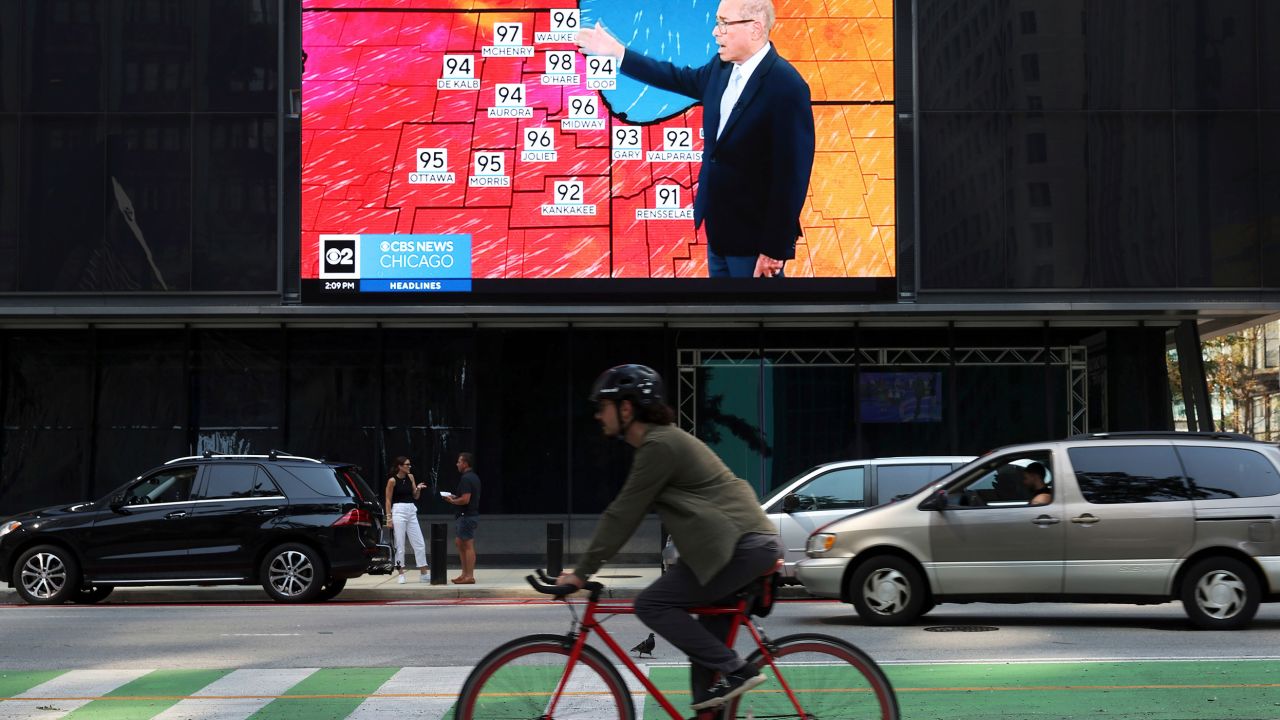 A bicyclist rides past a screen airing a weather report at Daley Plaza in Chicago in August.
