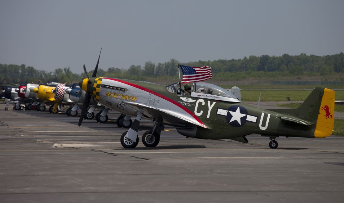 The pilot of a P51 Mustang waves the American flag after a practice flight with dozens of World War II era aircraft at Culpeper Regional Airport in Brandy Station, Virginia, May 7, 2015. Dozens of World War II era planes will fly past the National Mall in Washington, DC, on May 8, during the Arsenal of Democracy World War II Victory Capitol Flyover to commemorate the 70th anniversary of Victory in Europe (VE) Day. AFP PHOTO / ANDREW CABALLERO-REYNOLDS (Photo credit should read Andrew Caballero-Reynolds/AFP via Getty Images)
