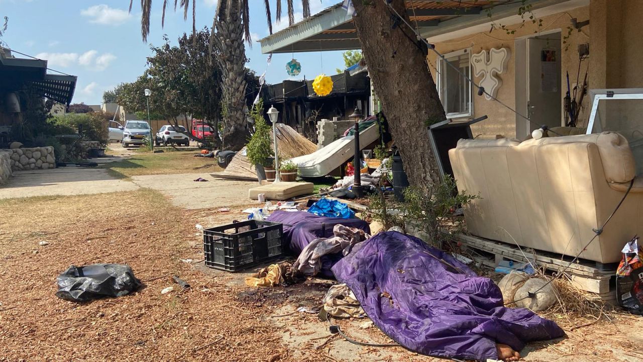 A covered body is seen lying on the ground in Kfar Aza. 