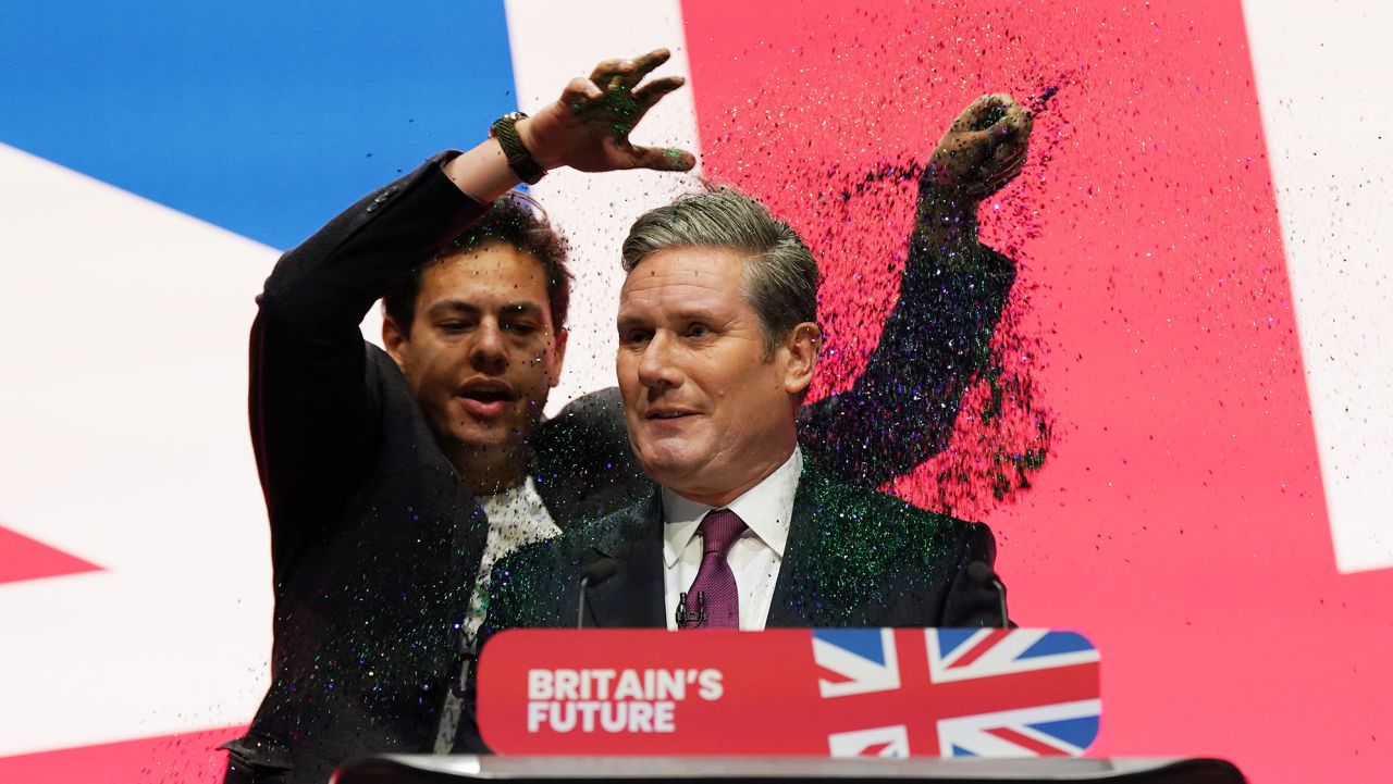 LIVERPOOL, ENGLAND - OCTOBER 10: A protestor storms the stage and throws glitter over Labour party leader, Sir Keir Starmer during the leader's speech on the third day of the Labour Party conference on October 10, 2023 in Liverpool, England. Labour leader Sir Keir Starmer will later address delegates and party members at the annual Labour Party Conference in the Liverpool Conference Centre. Keir Starmer will pledge to give more powers to local authorities and mayors and to 'build a new Britain' accelerating the building of new homes on unused urban land. (Photo by CIan Forsyth/Getty Images)