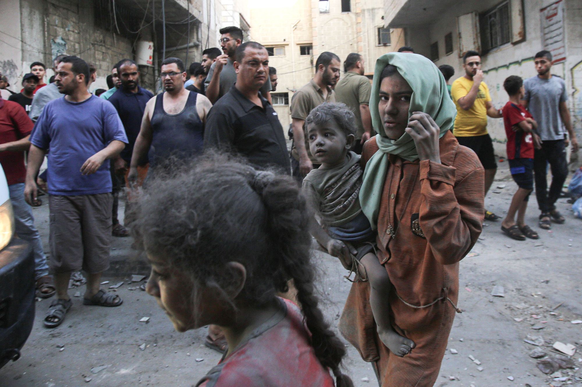 A Palestinian woman covered in dust and dirt carries a child in Gaza City on October 12.