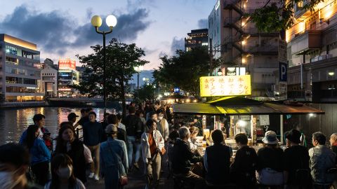 2R9H2PT Fukuoka, Japan - May 20 2023: People enjoy traditional street food in the Fukuoka night market along the Naka river in Kyushu in Japan