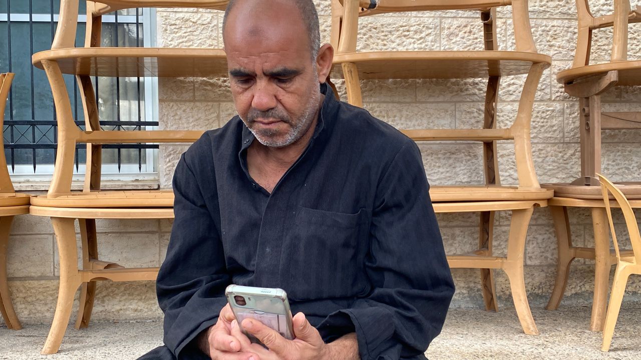 Marwan Saqer mira su teléfono mientras su familia intenta llamarlo desde Gaza, pero no logra comunicarse.
