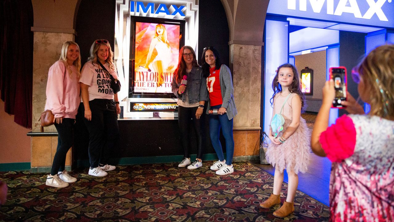 A young Taylor Swift fan takes a photo of the moms of their group next to the "Taylor Swift: The Eras Tour" poster before they go in to see the movie at Malco Paradiso Cinema Grill and IMAX in Memphis, Tenn., on Saturday, October 14, 2023.