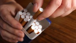 Woman taking cigarette out of pack at wooden table, closeup