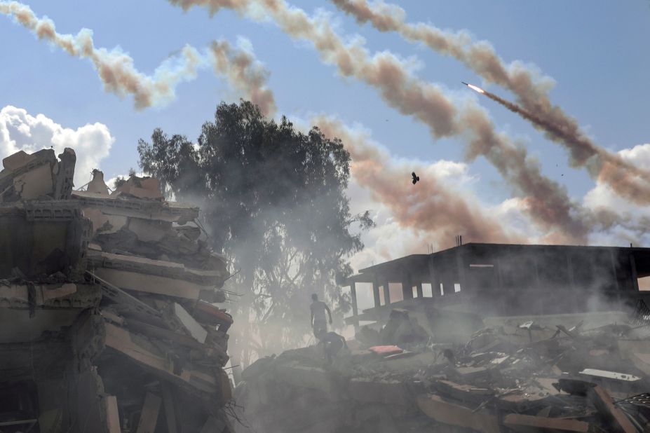 People walk through the rubble of destroyed buildings in Gaza City as rockets are fired overhead towards Israel on Thursday, October 19.