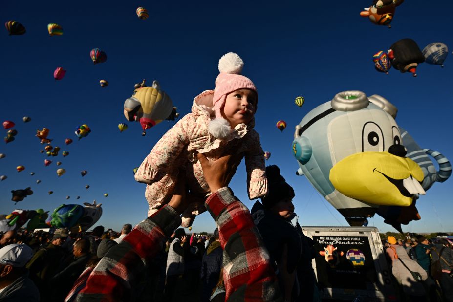 A child is lifted into the air by her father as hot air balloons take flight during the Albuquerque International Balloon Fiesta in Albuquerque, New Mexico, on Friday, October 13.