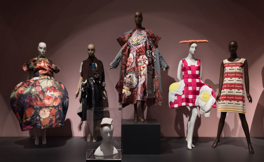Pieces included in the exhibition's "Feeding the Eye" display include a sculptural gown from Comme des Garçons Spring-Summer 2018 collection (far left),  a PB&J sandwich hat designed by Stephen Jones (foreground center) and the paper "Souper Dress" designed by Campbell's Soup Company circa-1966 (far right).