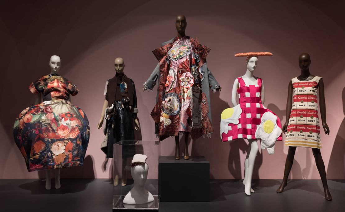Pieces included in the exhibition's "Feeding the Eye" display include a sculptural gown from Comme des Gar?ons Spring-Summer 2018 collection (far left), a PB&J sandwich hat designed by Stephen Jones (foreground center) and the paper "Souper Dress" designed by Campbell's Soup Company circa-1966 (far right).