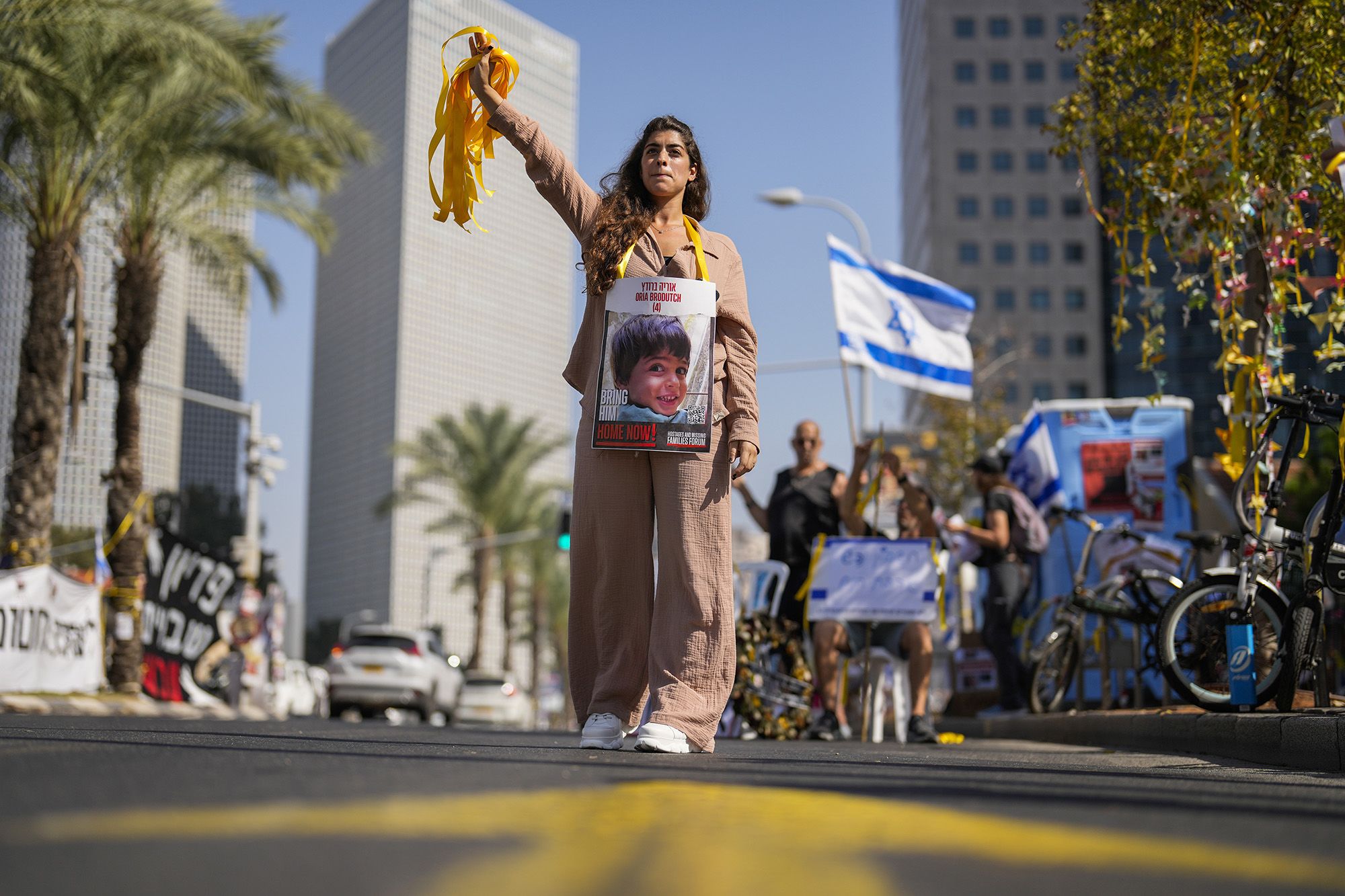 A woman with a photograph of a child who was abducted during the Hamas attack on Israel hands out yellow ribbons to passing drivers in central Tel Aviv, Israel, on October 25.<br /> 