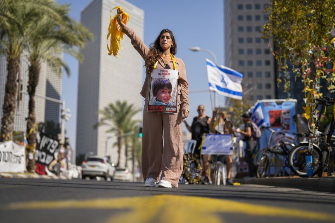 A woman with a photograph of a child who was abducted during the Hamas attack on Israel hands out yellow ribbons to passing drivers in central Tel Aviv, Israel, on October 25.<br /> 