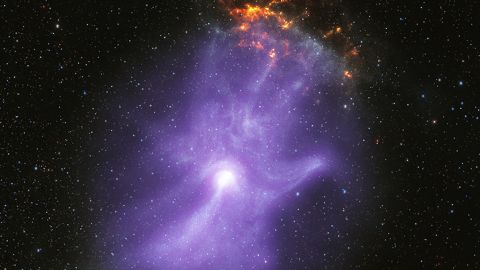 This release features a composite image of a pulsar wind nebula, which strongly resembles a ghostly purple hand with sparkling fingertips.
A pulsar is a highly magnetized collapsed star that rotates and creates jets of matter flowing away from its poles. These jets, along with intense winds of particles, form pulsar wind nebulae. Here, the pulsar wind nebula known as MSH 15-52 resembles a hazy purple cloud set against a black, starry backdrop. Both NASA's Chandra X-ray Observatory and the Imaging X-ray Polarimetry Explorer (IXPE) have observed MSH 15-52. Their observations revealed that the shape of this pulsar wind nebula strongly resembles a human hand, including five fingers, a palm and wrist. The bright white spot near the base of the palm is the pulsar itself. The three longest fingertips of the hand-shape point toward our upper right, or 1:00 on a clock face. There, a small, mottled, orange and yellow cloud appears to sparkle or glow like embers. This orange cloud is part of the remains of the supernova explosion that created the pulsar. The backdrop of stars was captured in infrared light.