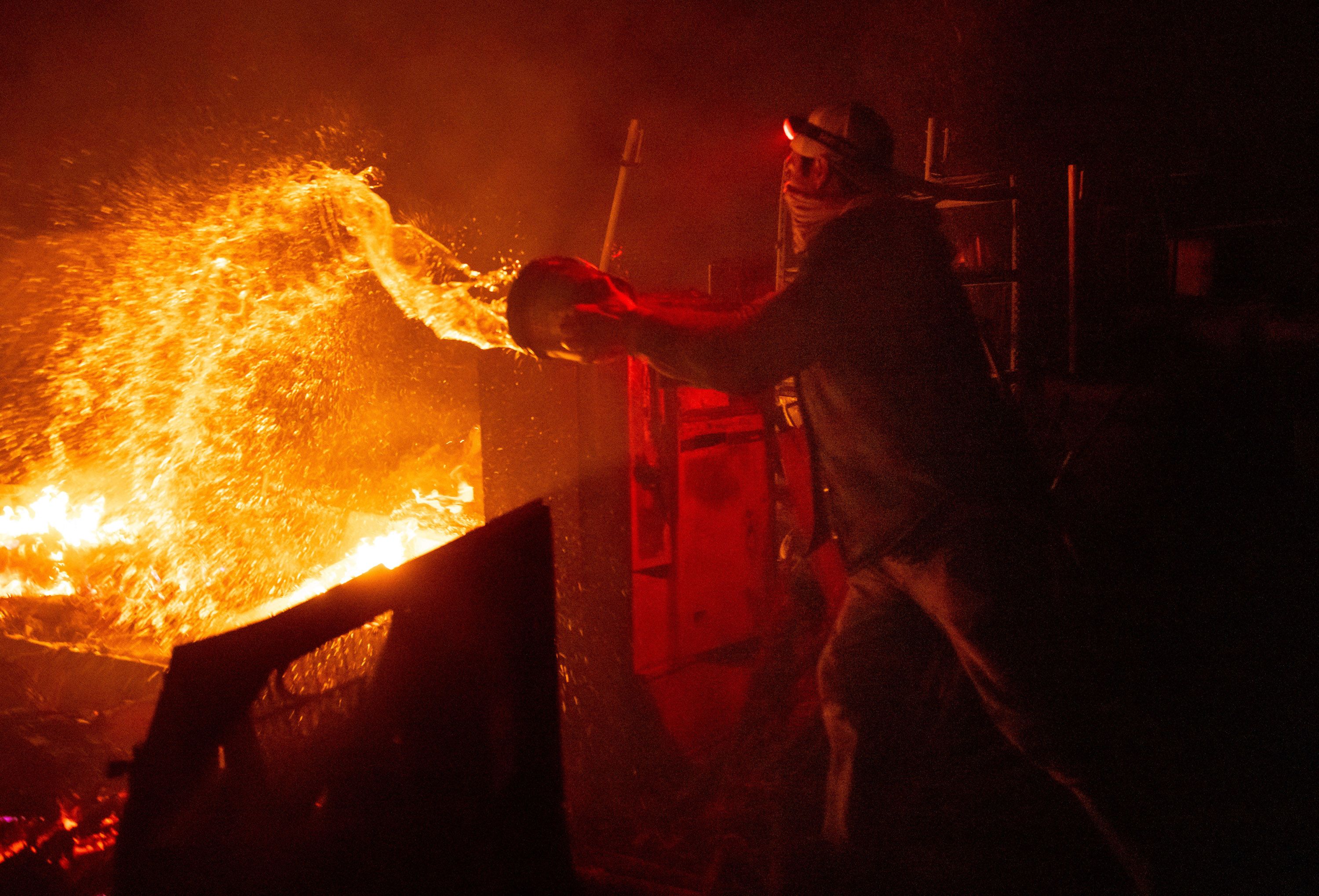 Francis Lopez douses flames with a bucket of water as the Highland Fire burns through his property in Aguanga, California, on Monday, October 30. As of early Tuesday morning, the fire had charred 2,200 acres of land.