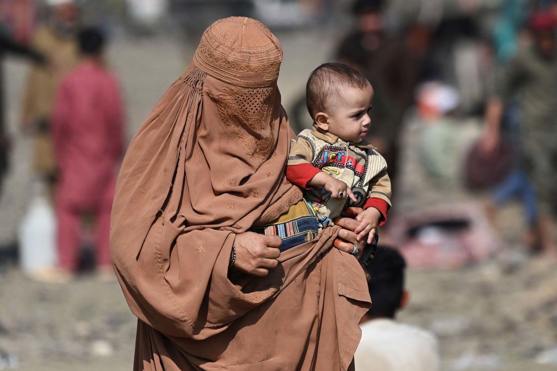 TOPSHOT - An Afghan refugee with her child who arrived from Pakistan walk at a makeshift camp near the Afghanistan-Pakistan Torkham border in Nangarhar province on November 2, 2023. More than 165,000 Afghans have fled Pakistan since Islamabad issued an ultimatum to 1.7 million people a month ago to leave or face arrest and deportation, officials said on November 2. (Photo by Wakil KOHSAR / AFP) (Photo by WAKIL KOHSAR/AFP via Getty Images)