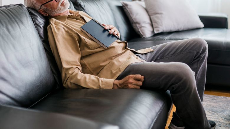 Senior man taking a nap at home after reading.